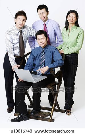 Stock Image - Portrait of a businessman holding a laptop with three businesspeople standing beside him. Fotosearch