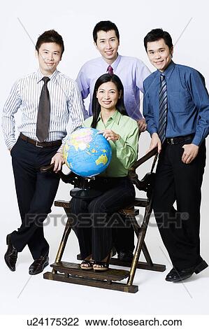 Stock Image - Portrait of a businesswoman holding a globe with three businessmen standing beside her. Fotosearch