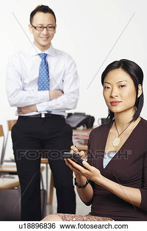 Portrait of a businesswoman holding a personal data assistant with a businessman standing behind her View Large Photo Image Stock Photograph - Portrait of a businesswoman holding a personal data assistant with a businessman standing behind her. Fotosearch