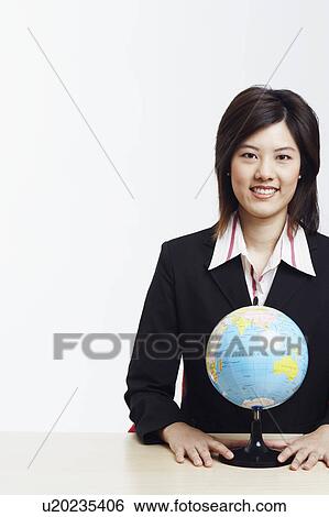 Stock Photograph - Portrait of a businesswoman sitting with a globe in front of her. Fotosearch