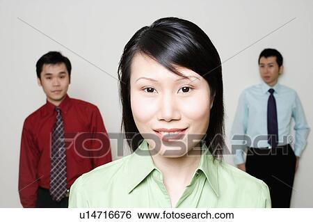 Stock Photograph - Portrait of a businesswoman smiling with two businessmen standing behind her. Fotosearch