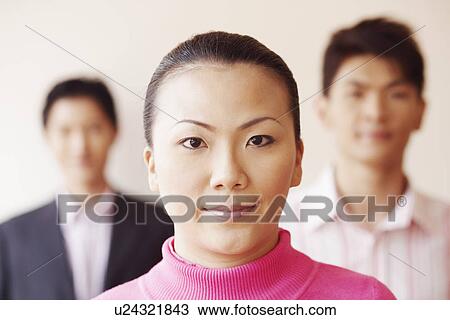 Stock Image - Portrait of a businesswoman with two businessmen in the background. Fotosearch