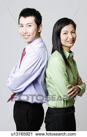 Stock Image - Side profile of a young businessman and a businesswoman standing back to back. Fotosearch