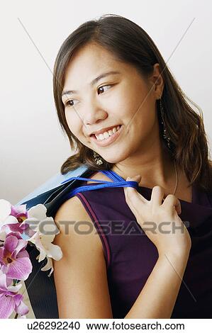 Stock Image - Close-up of a young woman carrying flowers and shopping bags. Fotosearch