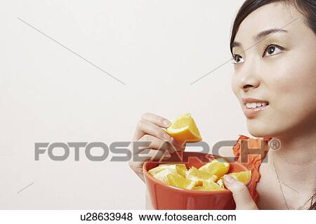 Stock Photo - Close-up of a young woman holding a slice of orange. Fotosearch