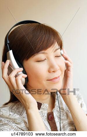 Stock Image - Close-up of a young woman wearing headphones and listening to music. Fotosearch