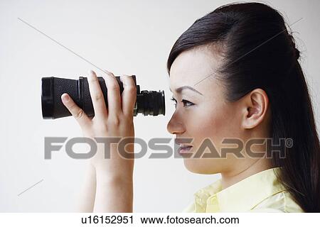 Stock Image - Side profile of a mid adult woman looking through a pair of binoculars. Fotosearch