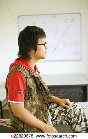 Stock Photo - Side profile of a teenage boy sitting on a desk in a classroom. Fotosearch