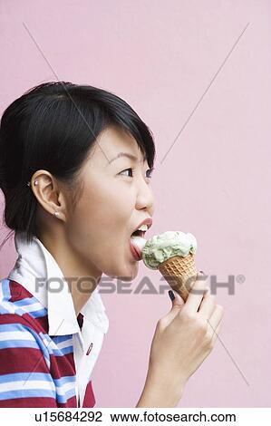 Stock Image - Side profile of a young woman eating an ice-cream cone. Fotosearch
