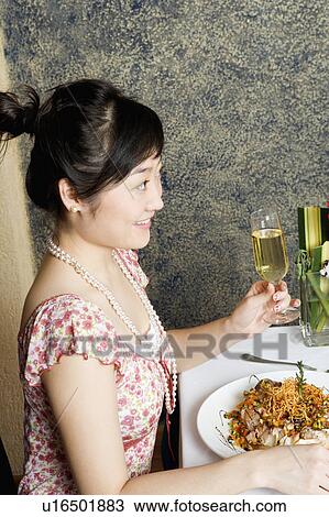Stock Image - Side profile of a young woman holding a glass of champagne. Fotosearch