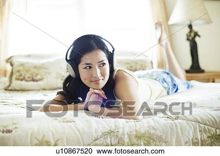 A woman listening to music laying on bed View Large Photo Image Stock Image - A woman listening to music laying on bed. Fotosearch