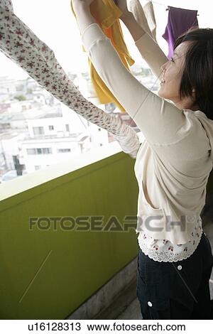 Stock Image - A young woman dries clothes on the clothesline at the balcony. Fotosearch