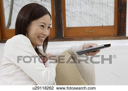View of a young woman holding a remote control View Large Photo Image Stock Image - View of a young woman holding a remote control. Fotosearch