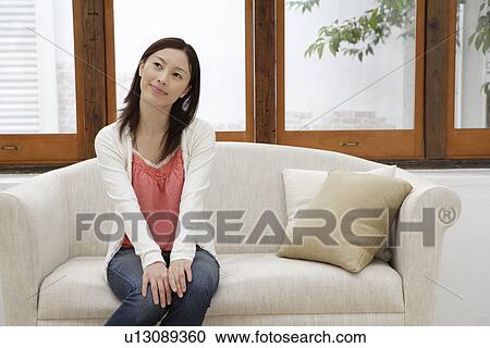 Stock Image - View of a young woman sitting on a sofa. Fotosearch