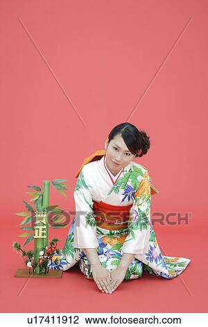 Stock Image - View of teenage girl in traditional outfit beside a plant. Fotosearch