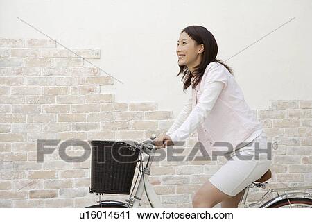 Stock Image - Side view of a young woman bicycling. Fotosearch