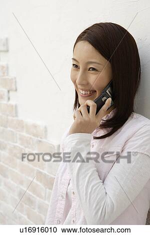 Stock Image - Side view of a young woman using cellphone. Fotosearch