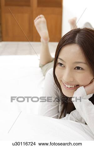 Picture - View of a cheerful woman lying on a bed. Fotosearch