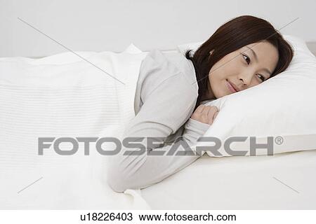 Stock Image - View of a young woman lying on a bed. Fotosearch