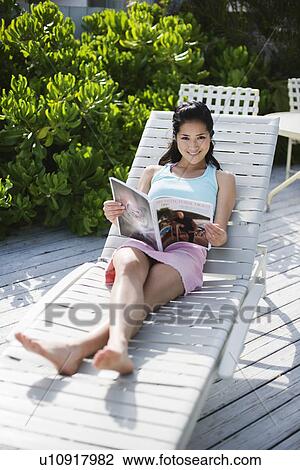 Stock Image - A woman on deck chair reading magazine. Fotosearch