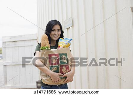 Stock Photograph - Portrait of a woman holding groceries with paper bag. Fotosearch