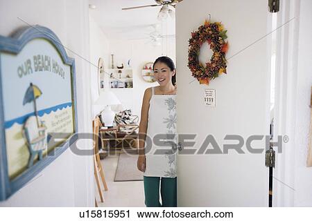 Stock Image - Portrait of a young woman standing by door. Fotosearch