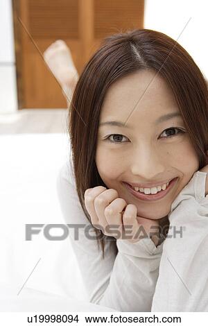 Picture - View of a cheerful woman lying on a bed. Fotosearch