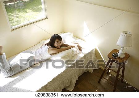 Young woman lying on bed View Large Photo Image Stock Image - Young woman lying on bed. Fotosearch