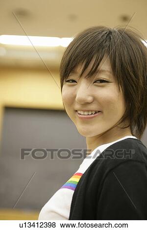 Stock Photo - A young woman smiles as she stares at the camera. Fotosearch
