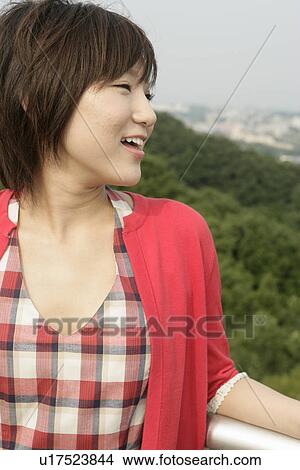 Picture - A young woman smiles heartily as she stands against the railing. Fotosearch