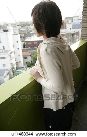 A young woman stands against the railing of the balcony as she enjoys the view of cityscape View Large Photo Image Picture - A young woman stands against the railing of the balcony as she enjoys the view of cityscape. Fotosearch