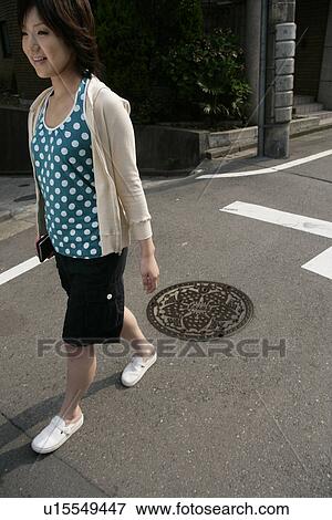 Stock Photo - A young woman walks by a manhole near the junction. Fotosearch