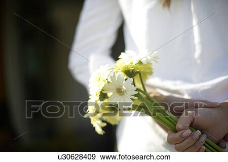 Stock Photo - Rear view of a young woman holding flowers. Fotosearch