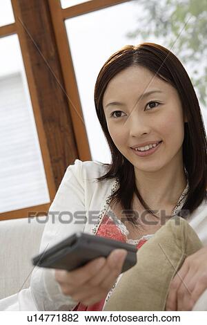 Stock Image - View of a young woman holding a remote control. Fotosearch