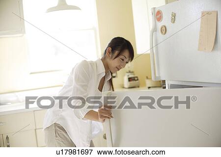 Stock Photo - View of a young woman opening refrigerator in kitchen. Fotosearch