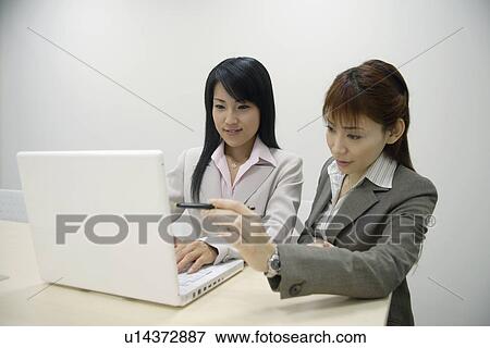 Two businesswomen working on the laptop together View Large Photo Image Stock Photo - Two businesswomen working on the laptop together. Fotosearch