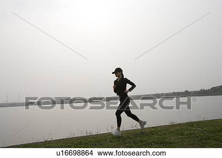 Picture - View of a young woman jogging beside a river. Fotosearch
