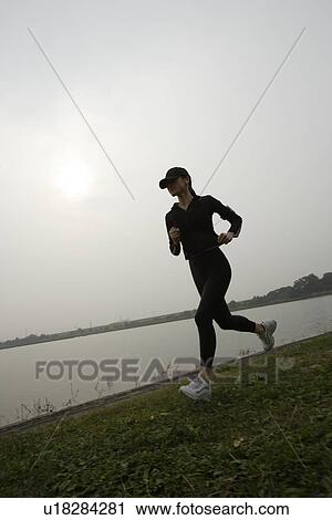 View of a young woman jogging beside a river View Large Photo Image Stock Image - View of a young woman jogging beside a river. Fotosearch