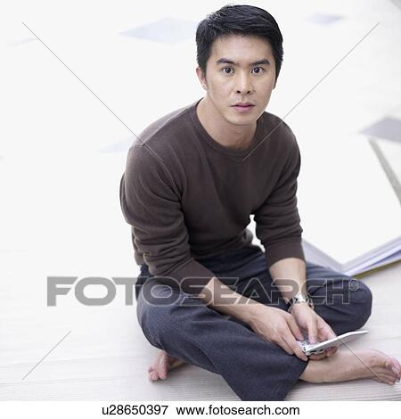 Stock Photo - High angle view of a young man sitting on the floor holding a mobile phone. Fotosearch