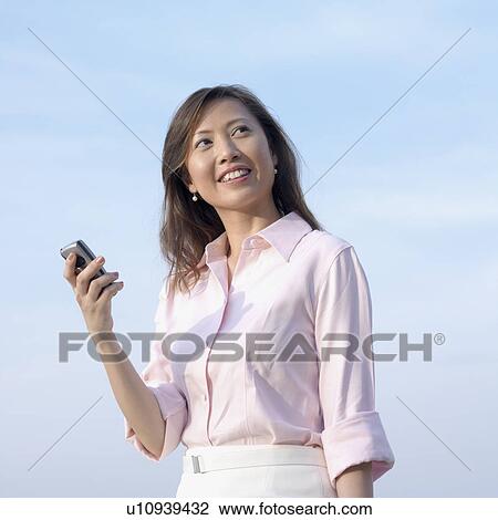 Stock Image - Low angle view of a mid adult woman holding a mobile phone. Fotosearch