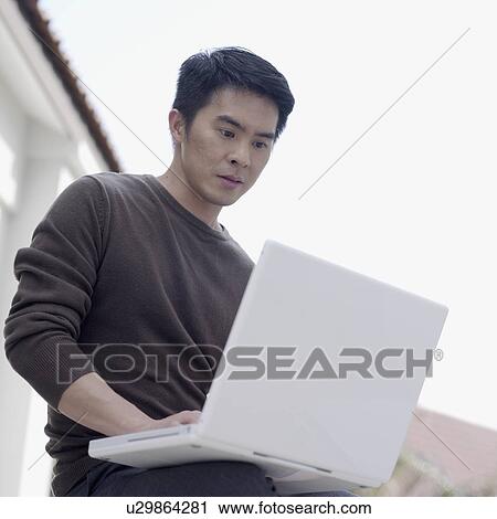 Stock Image - Low angle view of a young man using a laptop. Fotosearch