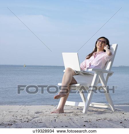 Picture - Mid adult woman talking on a mobile phone at the beach. Fotosearch