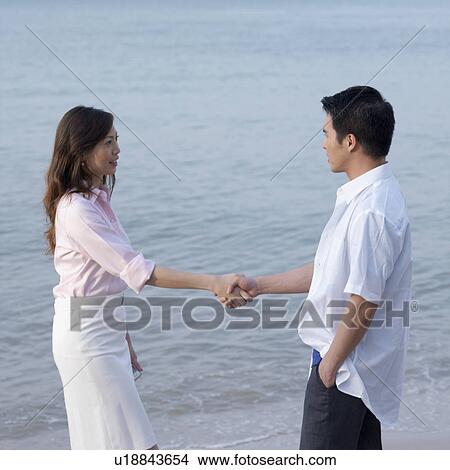 Picture - Side profile of a mid adult man and a mid adult woman shaking hands. Fotosearch