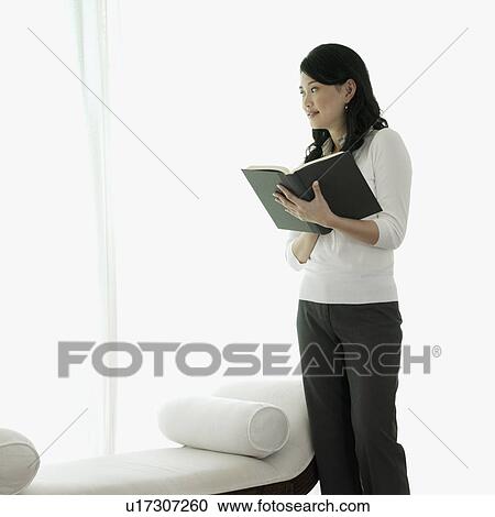 Stock Image - Young woman standing with a book in her hand. Fotosearch