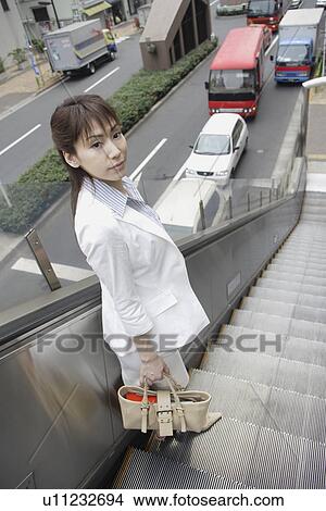 Picture - A formally dressed woman stands on the escalators. Fotosearch