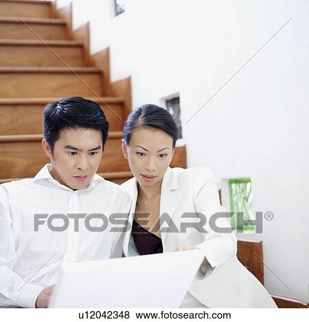 Businessman and businesswoman sitting on a staircase and looking at a laptop View Large Photo Image Stock Photo - Businessman and businesswoman sitting on a staircase and looking at a laptop. Fotosearch