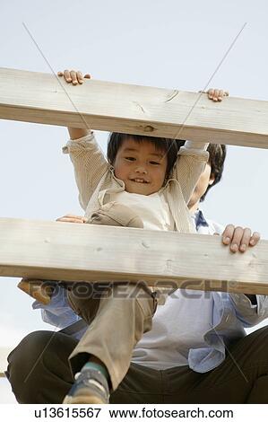 Stock Photo - A small boy leaping out of the wooden railing as his father holds him. Fotosearch