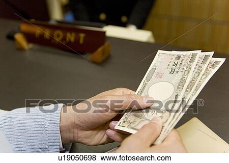Man at the reception in the hotel, holding Yen bills, close up View Large Photo Image Stock Photo - Man at the reception in the hotel, holding Yen bills, close up. Fotosearch