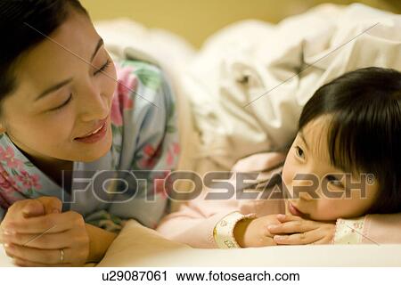 Stock Image - Mid adult woman and girl on Futon, smiling. Fotosearch