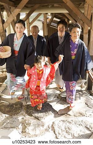Stock Image - Multi-generation family in Yukata walking in corridor, smiling. Fotosearch